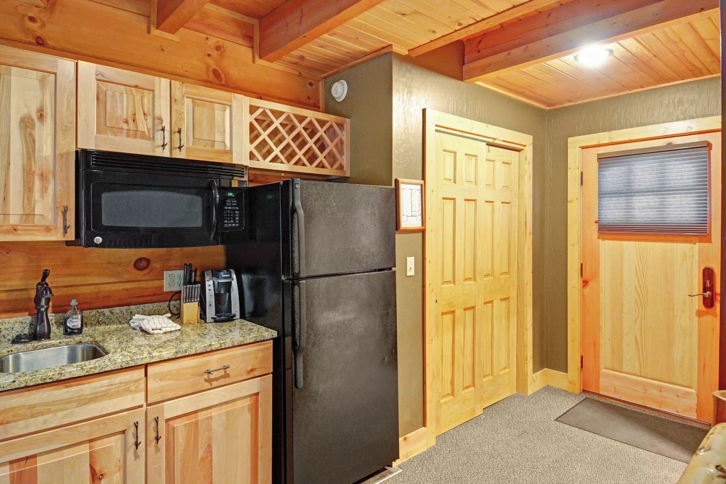 A compact kitchen with wooden cabinets, a black refrigerator, a microwave, and a coffee maker.