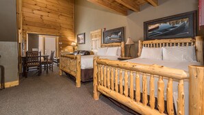 A wooden cabin-style room with two beds, a dining area, and a view of the mountains. - Mountainside Loft Cabin 46R (McHenry)