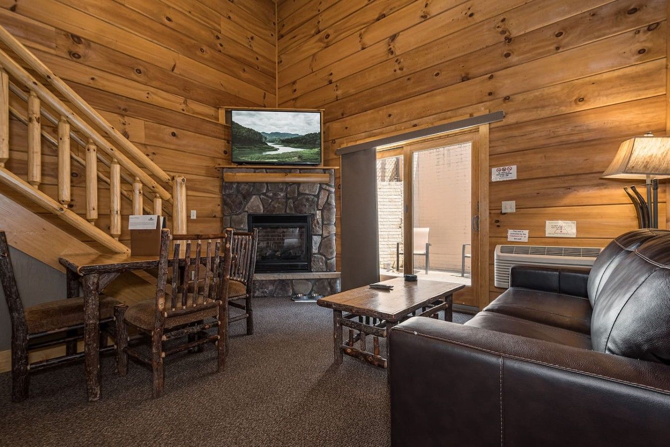 A wooden interior with a fireplace, a television, a sofa, and a dining table with chairs.