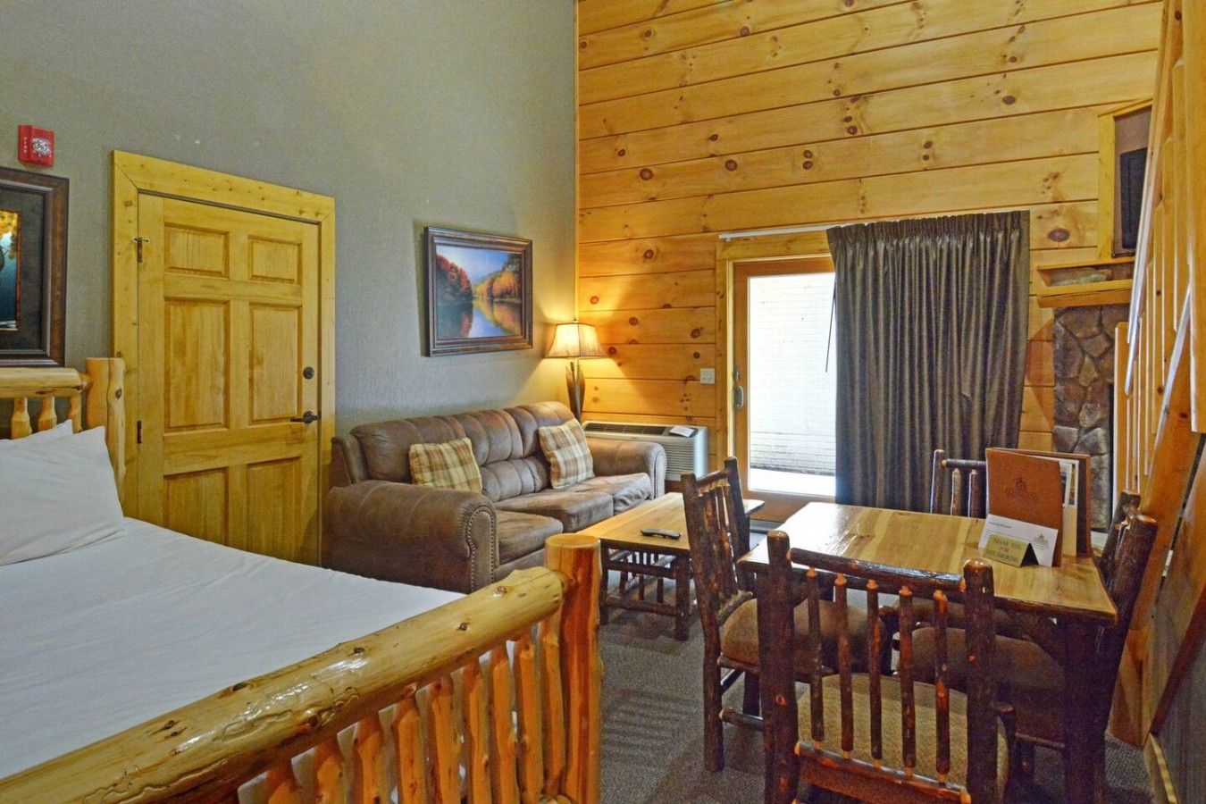 A cozy room with a bed, a sofa, a dining table with chairs, a lamp, and a painting on the wall.