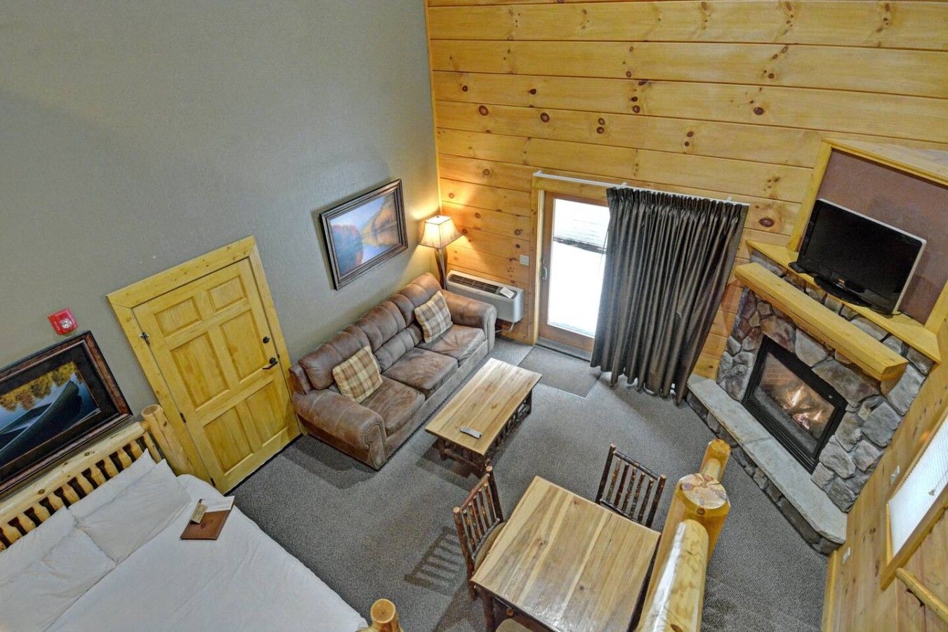 A cozy cabin interior with a sofa, a table, a fireplace, and a television.