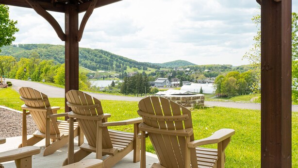 A wooden gazebo with Adirondack chairs overlooking a scenic landscape with hills and a lake. - Mountainside Loft Cabin 46R (McHenry)