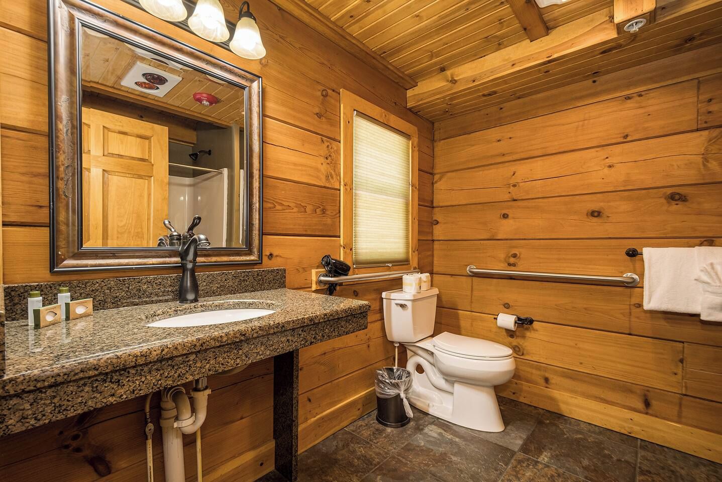 A wooden bathroom with a granite countertop, a toilet, a mirror, and a towel rack.