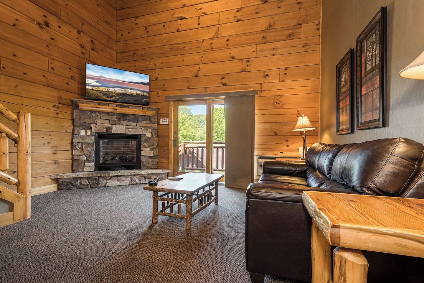 A wooden interior with a stone fireplace, a leather sofa, a television, and a wooden table.