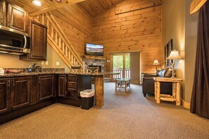 A log cabin interior with a kitchen, dining area, and a stone fireplace.