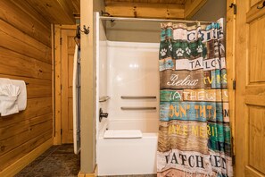 A wooden cabin bathroom with a white bathtub, a shower curtain with various text and images, and a towel hanging on the wall. - Mountainside Cabin 48, Family Suite-Hot Tub, Dog Friendly (McHenry)