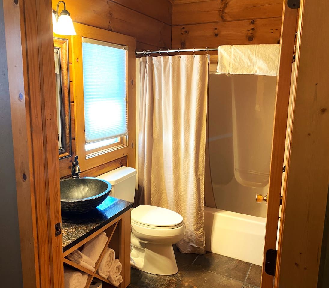 A wooden cabin bathroom with a sink, toilet, and shower.
