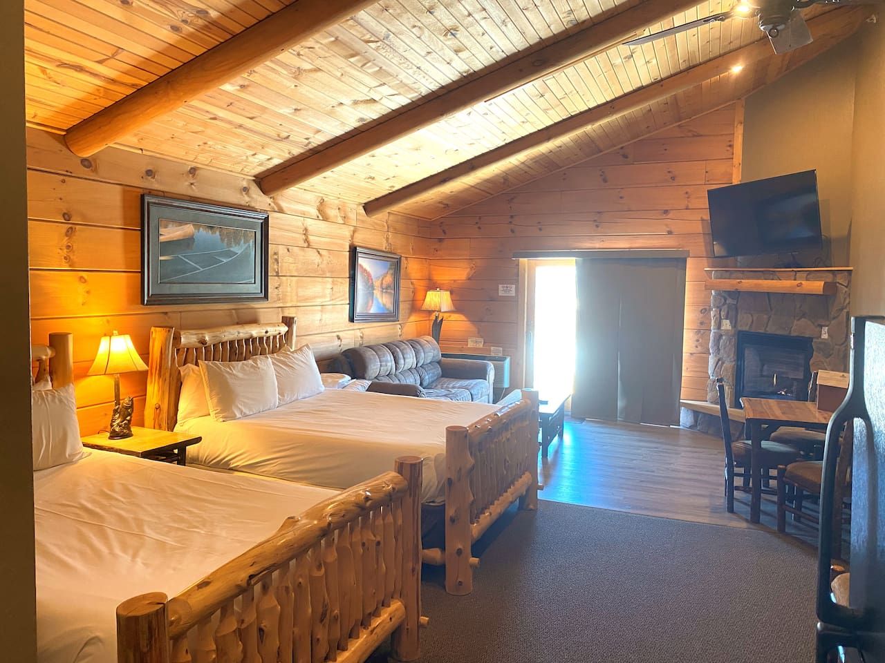 A log cabin room with two beds, a fireplace, and a television.