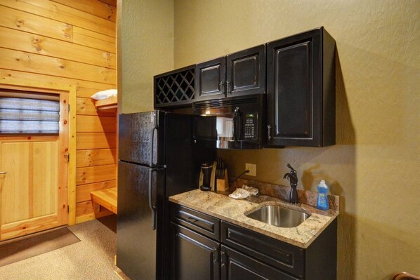 A compact kitchen with a refrigerator, microwave, sink, and wooden cabinets. - C49R - King Bed, Duplex (McHenry)