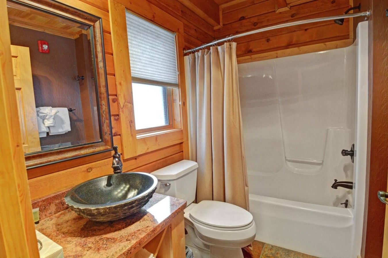 A bathroom with a wooden interior, a white toilet, a large sink with a bowl, and a bathtub with a shower curtain.
