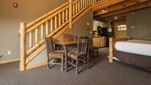 A wooden staircase leading to a loft bedroom with a bed, a dining table with chairs, and a kitchen area.