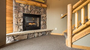 A stone fireplace with a built-in bench, a wooden staircase, and a view of autumn foliage.