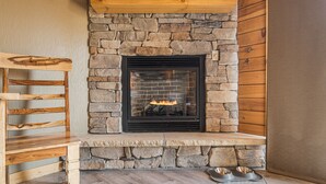 A stone fireplace with a black frame, a wooden bench, and a dog bowl on the floor.