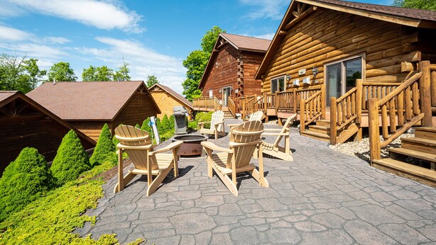 A log cabin with a patio area featuring Adirondack chairs and a fire pit.