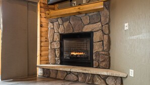 A stone fireplace with a built-in TV above it, set in a room with wooden walls and a stone accent wall. - Mountainside Cabin 51L (McHenry)