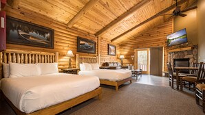 A log cabin room with two beds, a stone fireplace, a television, and a dining area. - Mountainside Cabin 51L (McHenry)