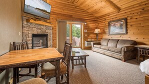 A cozy cabin interior with a stone fireplace, wooden dining table, and a leather sofa.