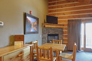 A wooden interior with a fireplace, a television mounted above it, and a dining area with wooden chairs and a table.