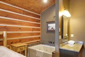 A wooden-paneled bathroom with a bathtub, a wooden stool, a framed picture on the wall, and a marble countertop with a mirror.