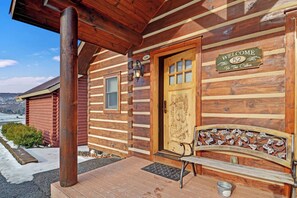 A log cabin with a wooden door, a welcome sign, and a bench outside. - C52L - King Bed, Bunk Bed, Duplex (McHenry)