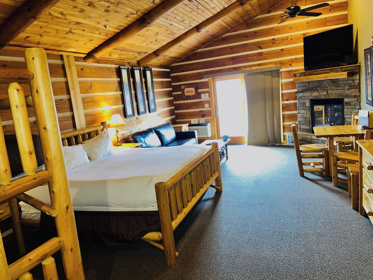 Interior de una cabaña de madera con una cama, comedor y chimenea.