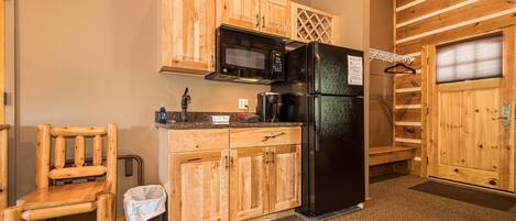 Una cocina compacta con armarios de madera, un refrigerador negro, un microondas y una cafetera.