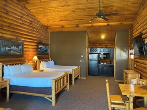 A log cabin-style room with two beds, a dining table, and a kitchenette.