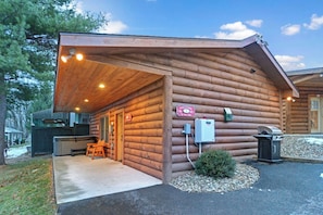 Eine Blockhütte mit Veranda, einem Willkommensschild, einem Grill und einem kleinen Busch.