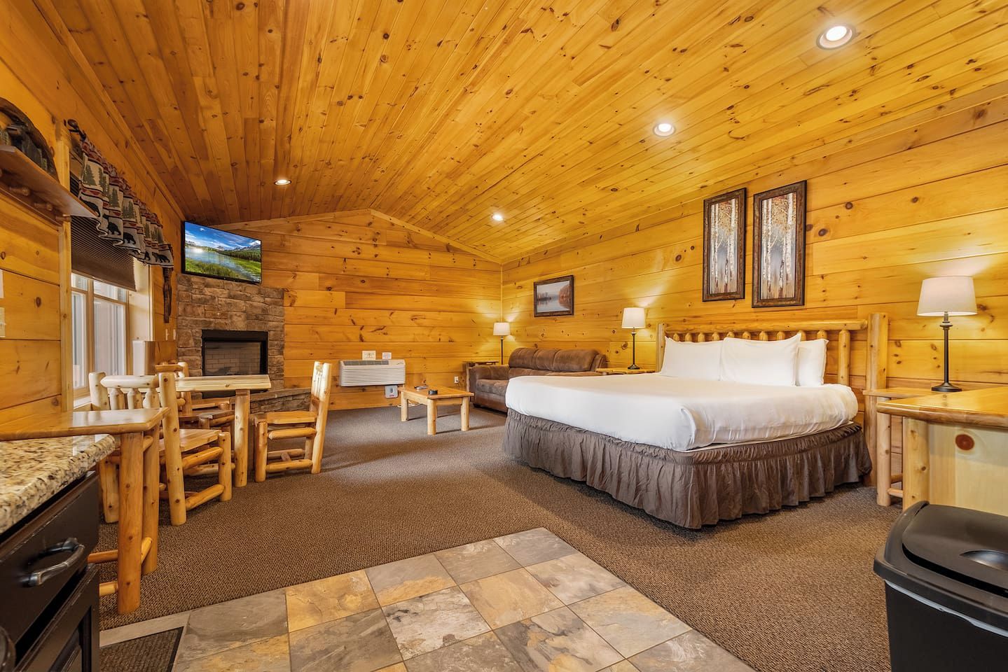 A log cabin room with a bed, a desk, a chair, a fireplace, and a television.