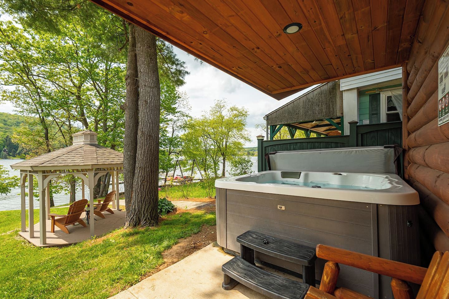 A hot tub, wooden deck, gazebo, and a view of a lake.
