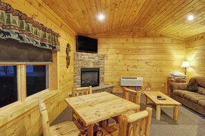 Ein gemütliches Blockhaus-Interieur mit Kamin aus Stein, Holzmöbeln und einem an der Wand befestigten Fernseher.