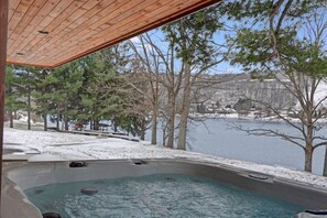 Ein Whirlpool mit Holzdach mit Blick auf eine verschneite Landschaft und ein Gewässer.