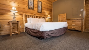 Een slaapkamer met houten lambrisering, een bed, twee nachtkastjes met lampen, een dressoir en een deur.