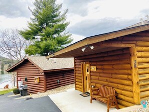 A log cabin with a porch, a grill, and a chair.