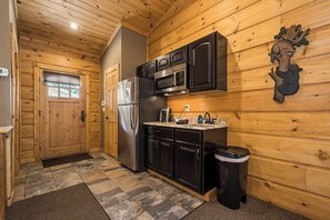 Une cuisine de taille réduite avec des murs en bois, un réfrigérateur, un four à micro-ondes et un évier.