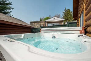 A hot tub in a backyard with a wooden deck and a house in the background.