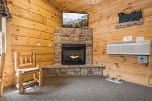 Un intérieur de chalet chaleureux avec une cheminée en pierre, un téléviseur fixé au mur et une décoration sur le thème des ours.