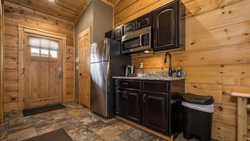 A compact kitchen with wooden walls, a refrigerator, a microwave, and a sink.