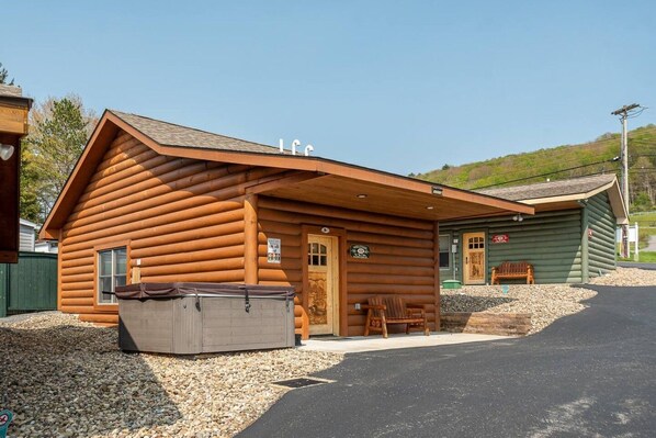 A log cabin with a front porch, a covered outdoor seating area, and a small shed.