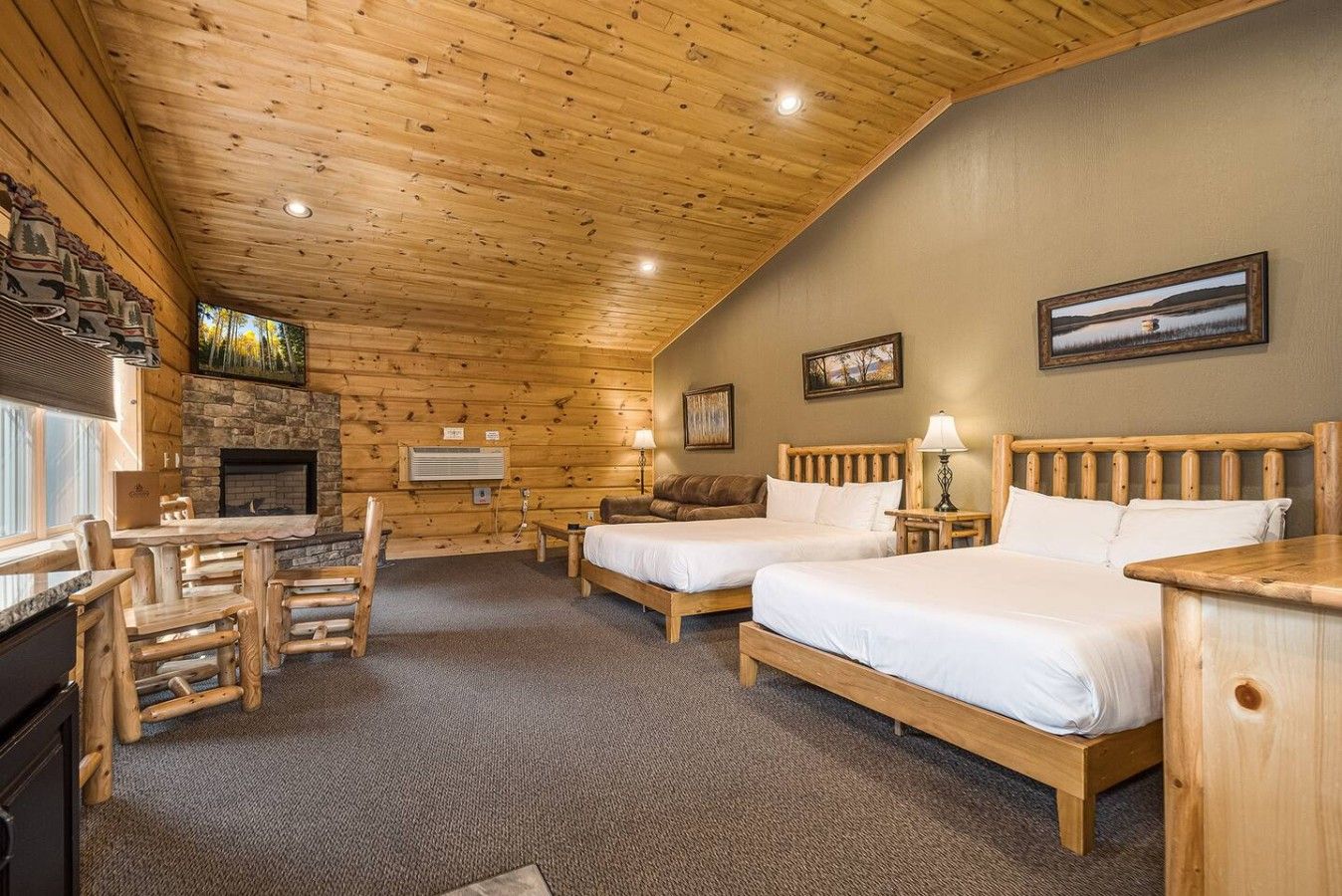 A log cabin-style room with two beds, a fireplace, a stone wall, and a dining area with wooden furniture.