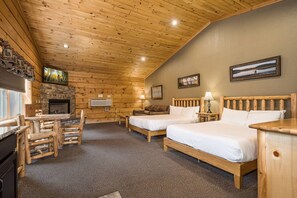 A log cabin-style room with two beds, a fireplace, a stone wall, and a dining area with wooden furniture. - C3 - 2 Queen, Lakefront, Hot Tub, Pet Friendly (McHenry)
