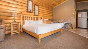 Un dormitorio de cabaña de madera con una cama de madera, una mesita de noche con una lámpara, un baño con bañera y un refrigerador.