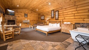Un dormitorio de cabaña de madera con chimenea de piedra, una cama, un escritorio y un baño.