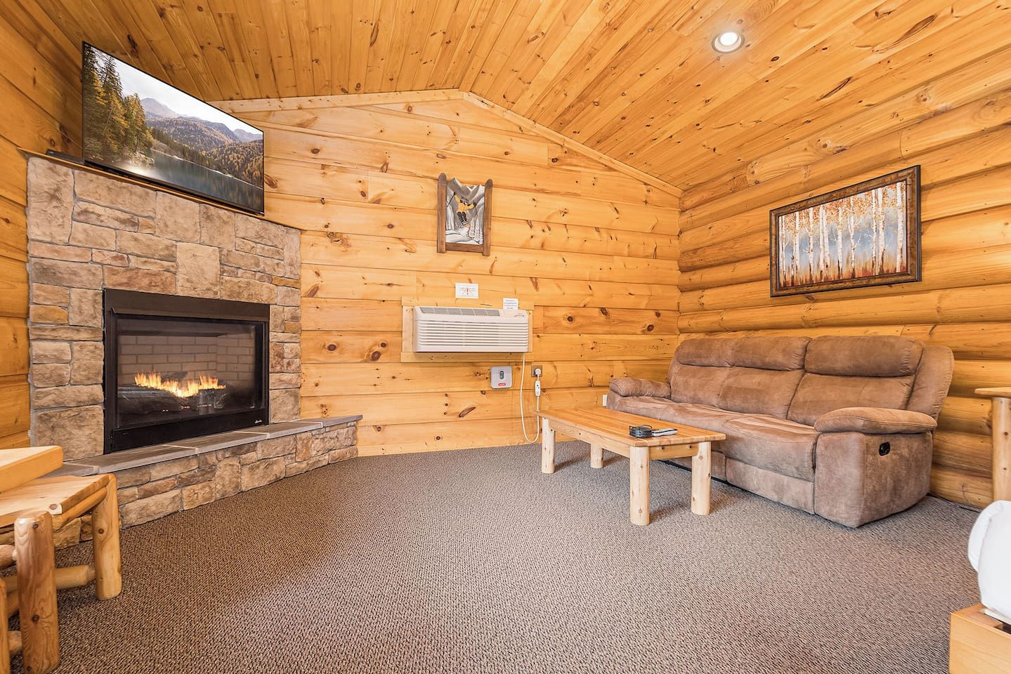 A log cabin interior with a stone fireplace, a sofa, a coffee table, and a painting on the wall.