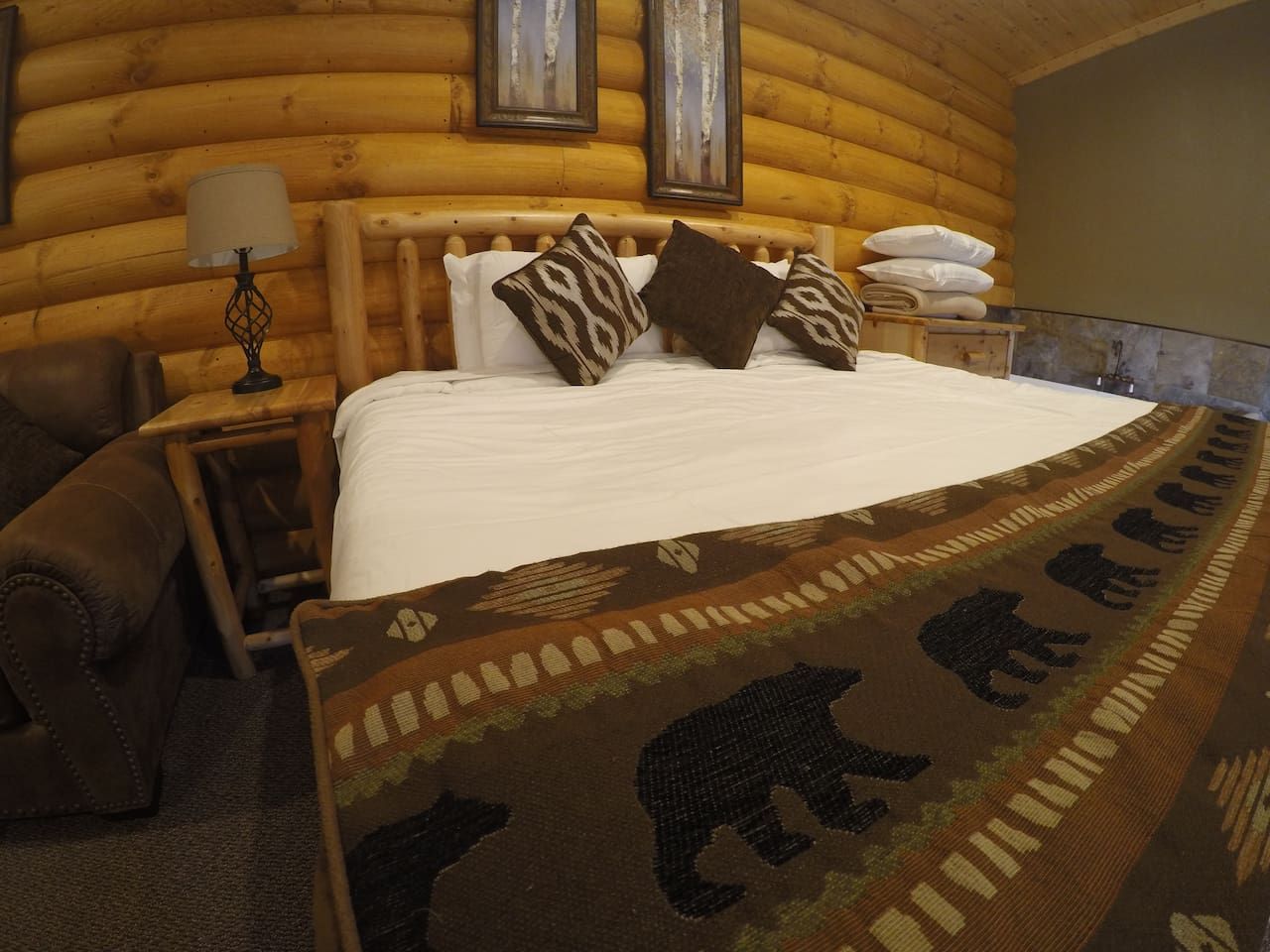 Une chambre dans un chalet en rondins, avec un lit, des oreillers, une lampe et une couverture à motifs d’ours.