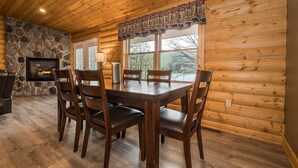 Un intérieur en bois avec une cheminée en pierre, une table à manger avec des chaises et de grandes fenêtres.