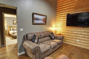 A living room with a leather sofa, a flat-screen TV mounted on a wooden wall, and a painting above the sofa.