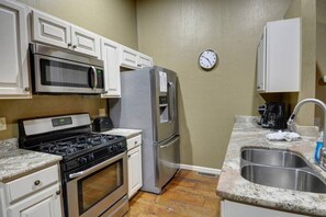 A kitchen with a stove, microwave, refrigerator, and a clock on the wall.