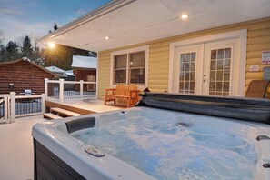 A hot tub on a covered deck, wooden chairs, and a cabin with a porch.