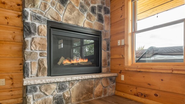 A stone fireplace with a glass door, wooden walls, and a window.